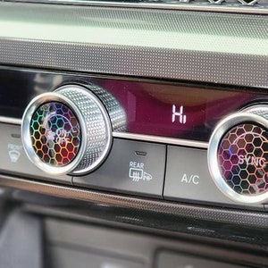 May include: Close-up of a car's climate control panel with three silver knobs. The knobs have a rainbow-colored honeycomb design and the text "SYNC" is visible on the rightmost knob.