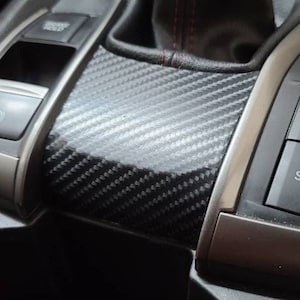 Puede incluir: Primer plano del interior de un coche con un panel de moldura de fibra de carbono negro y un botón con la etiqueta "SPORT".