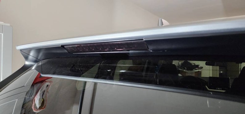May include: A silver car with a black rear window and a black rear spoiler with a red brake light.