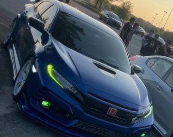 May include: A blue Honda Civic Type R with a black hood scoop and yellow headlights. The car is parked in a parking lot with other cars and people in the background.