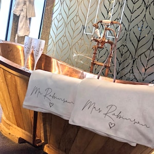 May include: A copper bathtub with two white towels, one with "Mr. Robinson" and the other with "Mrs. Robinson" embroidered on them. Two champagne flutes with "Mr. Robinson" and "Mrs. Robinson" on them are in the tub.