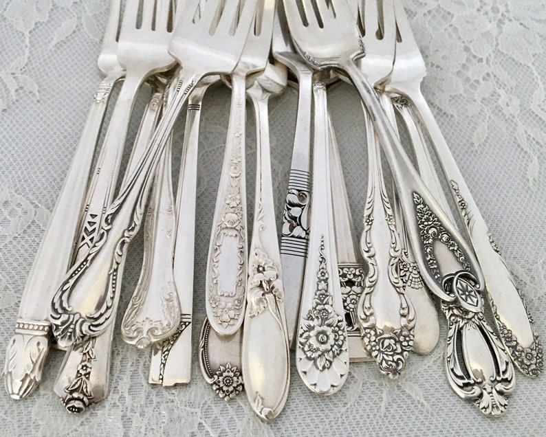 May include: A collection of antique silver forks with ornate, detailed designs. The forks vary in style, showcasing floral patterns, scrollwork, and geometric accents. The silver cutlery is arranged in a close-up shot, highlighting the intricate craftsmanship.