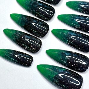 May include: A set of almond-shaped press-on nails featuring a gradient design that transitions from a deep black base to a vibrant green tip. The surface of each nail is finished with a glossy top coat and embedded with fine silver glitter particles.