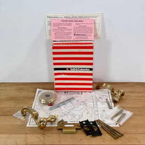 May include: A white ceramic mug with a black handle and the text "But First, Coffee" in a bold, black font. The mug is set against a blurred background, suggesting a cozy setting.