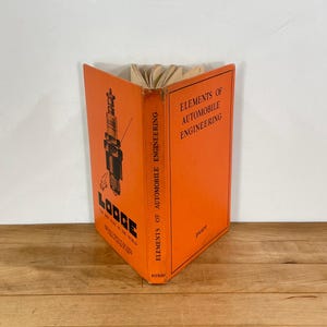 May include: A vintage orange hardcover book titled Elements of Automobile Engineering by Platt, published by Pitman. The front cover features a black graphic of a Lodge spark plug with the text Lodge The Best Plug In The World printed below.