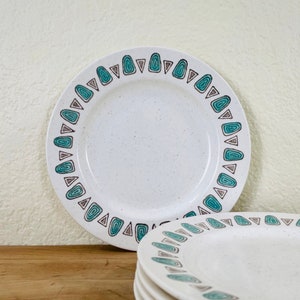 May include: White ceramic plates with a speckled finish and a teal and brown geometric border design. The plates are round and square, with a mid-century modern aesthetic. A set of dishes for serving food.