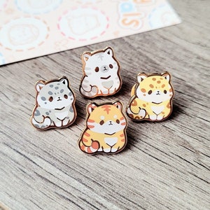 May include: Four enamel pins featuring different cartoon cats. The cats are all sitting down and have different colored fur. The pins are gold-colored and have a shiny finish.
