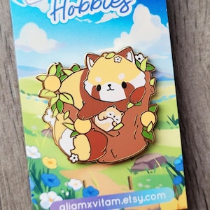May include: A pin featuring a red panda and baby nestled in a tree, surrounded by leaves and flowers. The pin has a gold outline and is set against a card with the text "Blossoming Hobbies" and a nature scene.