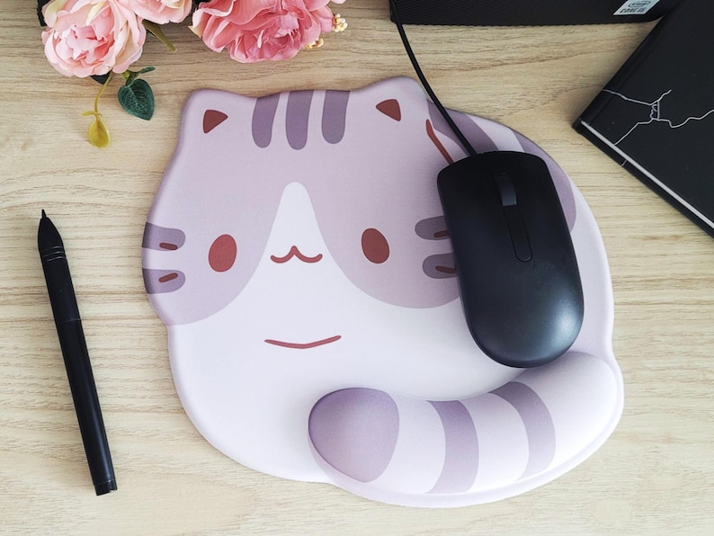 May include: A cat-shaped mousepad with a black mouse on top. The mousepad is light purple and white with a cat face design. A black stylus and a notebook are also visible.