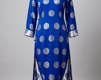 May include: A royal blue, long-sleeved dress with silver circular patterns. The dress features a mandarin collar, side slits, and silver trim on the cuffs and hem. The dress is displayed on a mannequin.