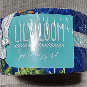 May include: A roll of fabric wrapped in clear plastic. The fabric has a blue floral pattern with green and orange accents. A teal tag reads "LILY LOOM" and "just for the joy of it."