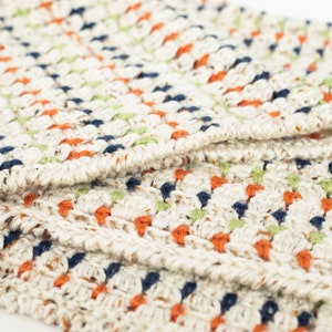May include: A close-up of a crocheted blanket with a textured pattern in shades of white, orange, green, and blue.
