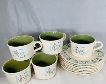 May include: A set of vintage cream-colored ceramic cups and saucers. The cups have a green interior and are decorated with blue and green geometric designs. The saucers have a matching design. A classic mid-century modern style.