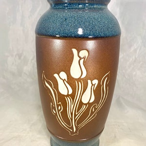 May include: A brown ceramic vase with a blue glaze at the top and bottom. The vase features a white design of stylised tulips.