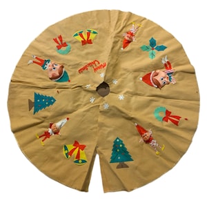 Könnte beinhalten: Beigefarbener Weihnachtsbaumrock mit gestickten Feiertagsmotiven. Mit Elfen, Glocken, Weihnachtsbäumen und den Worten "Merry Christmas". Eine festliche Weihnachtsdekoration im Vintage-Stil.