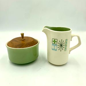 May include: A white ceramic mug with a black handle and the text "But First, Coffee" in a bold, black font. The mug is set against a blurred background, suggesting a cozy setting.