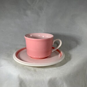 May include: A pink teacup and saucer set. The cup has a white rim and the saucer has a pink band around the edge.