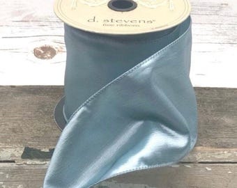 May include: A spool of light blue satin ribbon with the text "d. stevens fine ribbons" on the top. The ribbon is a soft, flowing material, perfect for crafts and decorations.