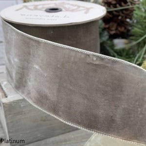 May include: A spool of platinum-colored velvet ribbon. The ribbon has a soft, plush texture and a stitched edge. The spool is partially visible, with the brand name printed on the top. The word "Platinum" is printed at the bottom of the image.