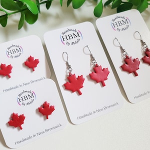 May include: Four cards with red maple leaf earrings on white cards. The cards have the text "Handmade HBM by Makaila" and "Handmade in New Brunswick".