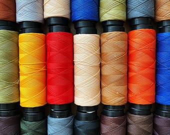 Może przedstawiać: Kolekcja szpul nici w różnych kolorach, w tym brązowym, czerwonym, pomarańczowym, żółtym, zielonym, niebieskim i szarym. Szpule są ułożone w rzędzie, z nicią nawiniętą wokół każdej szpuli.