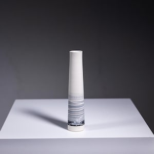 Può includere: Un vaso in ceramica bianca con un design astratto grigio e bianco. Il vaso è alto e sottile con un fondo arrotondato.