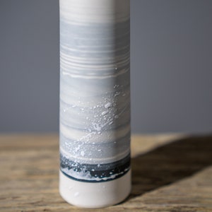 May include: A white ceramic vase with a grey and white striped pattern and white speckles. The vase has a dark blue band around the bottom.