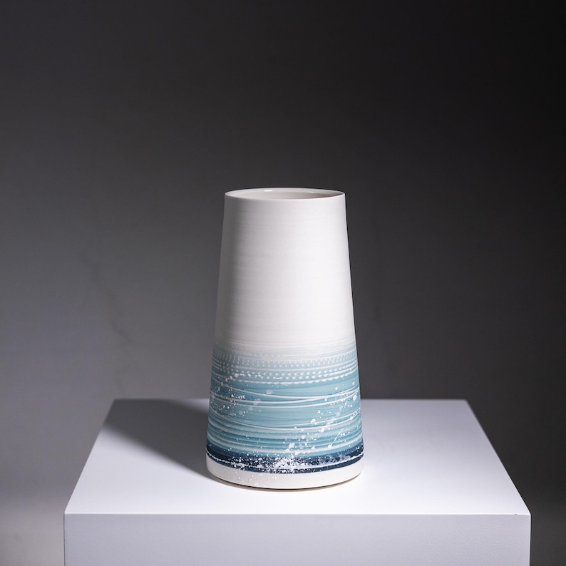 May include: A white ceramic vase with a blue and white patterned design. The vase has a wide base and a narrow neck.