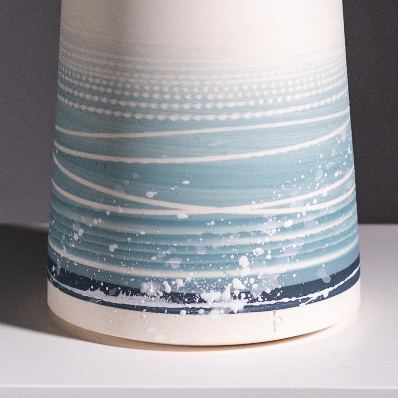 May include: A white ceramic vase with a blue and white abstract design. The design features wavy lines and white dots.