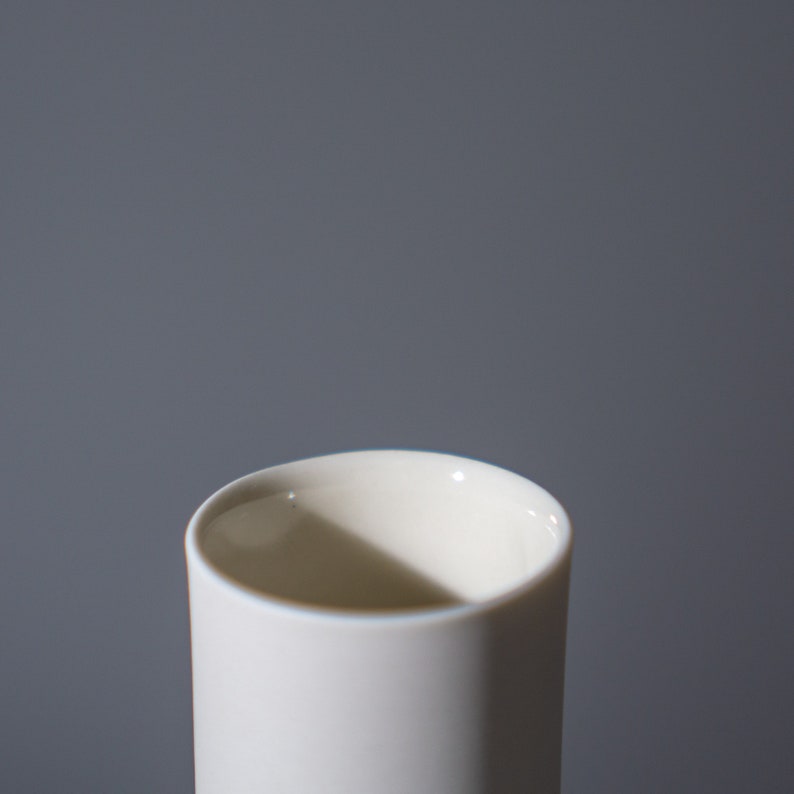 May include: A white ceramic cup with a smooth, rounded rim. The cup is empty and appears to be made of a thick, durable material.