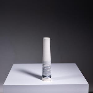 May include: A white ceramic vase with a grey and white geometric pattern. The vase is tall and slender, with a cylindrical shape.