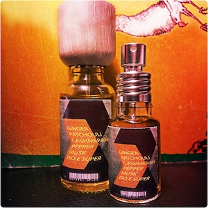 Pode incluir: Duas garrafas de vidro âmbar com rótulos pretos e tampas prateadas. Os rótulos listam os ingredientes: Gengibre, Patchouli, Cashmeran, Pimenta, Almíscar, Iso E Super.