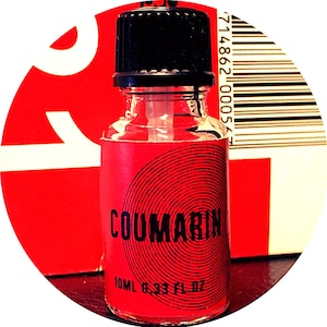 Op de afbeelding: Een kleine, heldere glazen fles met een zwarte dop en een rood etiket. Het etiket toont het woord "COUMARIN" in wit, met een cirkelvormig ontwerp. Bevat 10 ml vloeistof.