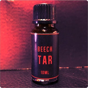 Könnte beinhalten: Eine kleine, dunkelbraune Glasflasche mit schwarzem Verschluss und Etikett. Das Etikett trägt die Aufschrift "Beech Tar" in roten Buchstaben und "10ML" in weißen Buchstaben.
