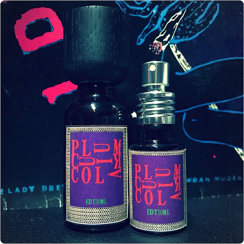 May include: Two glass bottles of perfume with black caps and purple labels. The labels read "Plum Cola" and have the text "EDT 30ML" and "EDT 10ML".
