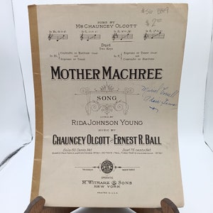Puede incluir: Una portada de partitura musical vintage para la canción "Mother Machree" de Chauncey Olcott y Ernest R. Ball. La portada presenta el título de la canción en letras grandes y en negrita, y los nombres del compositor y el letrista en una fuente más pequeña. La partitura está impresa en papel color crema con tinta negra.