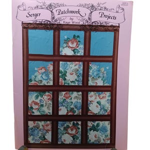 Könnte beinhalten: Eine rosa und weiße Broschüre mit dem Titel "Serger Patchwork Projects by Kaye Wood". Das Cover zeigt einen braunen Fensterrahmen mit 12 Quadraten aus Blumenstoff in Blautönen, Rosa und Weiß.