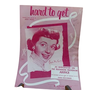 Könnte beinhalten: Ein rosa Notenblattcover mit dem Titel "hard to get" in weißen Buchstaben. Die Noten sind für ein Lied von Jack Segal und zeigen ein Schwarzweißfoto einer Frau mit einer Unterschrift, die "Gisele MacKenzie" lautet. Der Text "As introduced on the television program Justice" ist ebenfalls auf dem Cover enthalten.