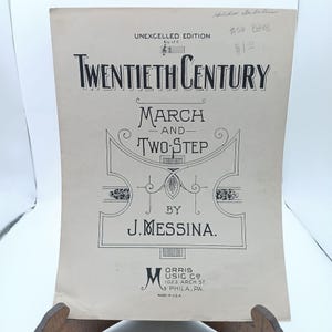 以下が含まれることがあります： J. メッシーナ作曲の「20世紀」というタイトルのマーチとツーステップのヴィンテージ楽譜の表紙。表紙は白地に黒インクで印刷されており、装飾的な枠が施されています。
