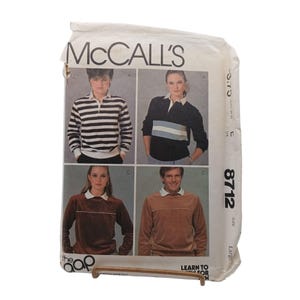 May include: Vintage McCall's sewing pattern packet featuring four different long-sleeve polo shirts. The shirts are in various colors, including black, brown, and a striped design. The packet has the text "McCall's" at the top and the number "8712" on the side.