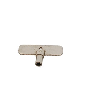 May include: A silver-toned metal winding key featuring a flat, rectangular handle with rounded corners and a small circular hole in the center. The key has a cylindrical shaft with a hollow opening at the base, designed for manual rotation.