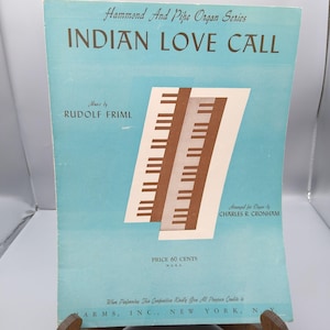 Puede incluir: Portada de partituras de "Indian Love Call" de la serie Hammond And Pipe Organ. La portada es azul claro con el título en letras grandes de color azul oscuro. Presenta una imagen estilizada de teclas de piano y el nombre del compositor.