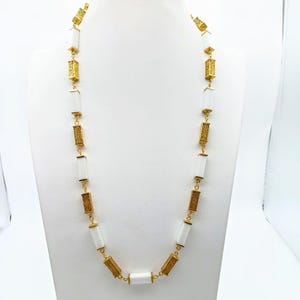 May include: A long gold chain necklace with white rectangular beads. Each bead has a gold patterned design.