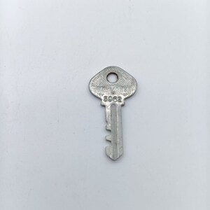 Puede incluir: Una llave plateada con una ranura para llave y una cabeza redonda. La cabeza está marcada con el texto "LAYMAKE" y el número "5962".