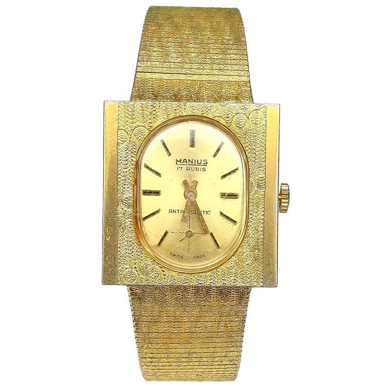 Puede incluir: Un reloj de pulsera dorado con una caja cuadrada y una esfera de forma ovalada. La esfera del reloj tiene agujas y marcadores negros, y el texto "MANIUS 17 RUBIS ANTISHOCK SWISS MADE" est&aacute; impreso en la esfera.