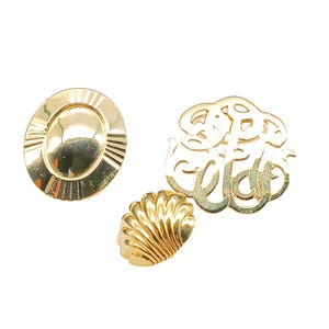 May include: Three gold-coloured metal buttons. One is round with a raised oval in the centre. Another is a shell shape. The third is a monogram with the letters "S.E.W." in a stylised font.