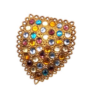 May include: A vintage gold-toned brooch in a heart shape, adorned with numerous colorful, round gemstones. The gemstones are in shades of blue, yellow, orange, purple, and clear. The brooch has a decorative, scalloped edge.