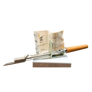 Puede incluir: Una herramienta vintage de metal y madera con un extremo puntiagudo y un mango de madera. La herramienta tiene un cuerpo de metal plateado y un mango de madera. La herramienta va acompañada de un pequeño folleto de instrucciones. El texto "EX DLE" es visible.