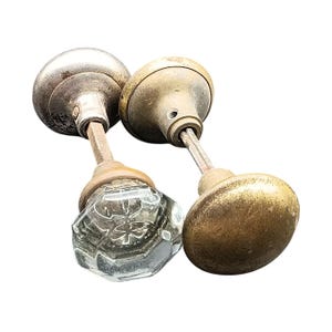 Peut inclure: Deux poignées de porte anciennes. L'une est un bouton en verre clair et facetté avec un motif floral. Les deux autres sont en métal, l'une avec une finition argentée et l'autre avec une finition en laiton. Les boutons montrent des signes d'âge et d'usure.