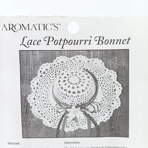 May include: A white crocheted lace potpourri bonnet. The bonnet is shaped like a sun hat with a wide brim and a small crown. The bonnet is decorated with a white ribbon and a small white flower.